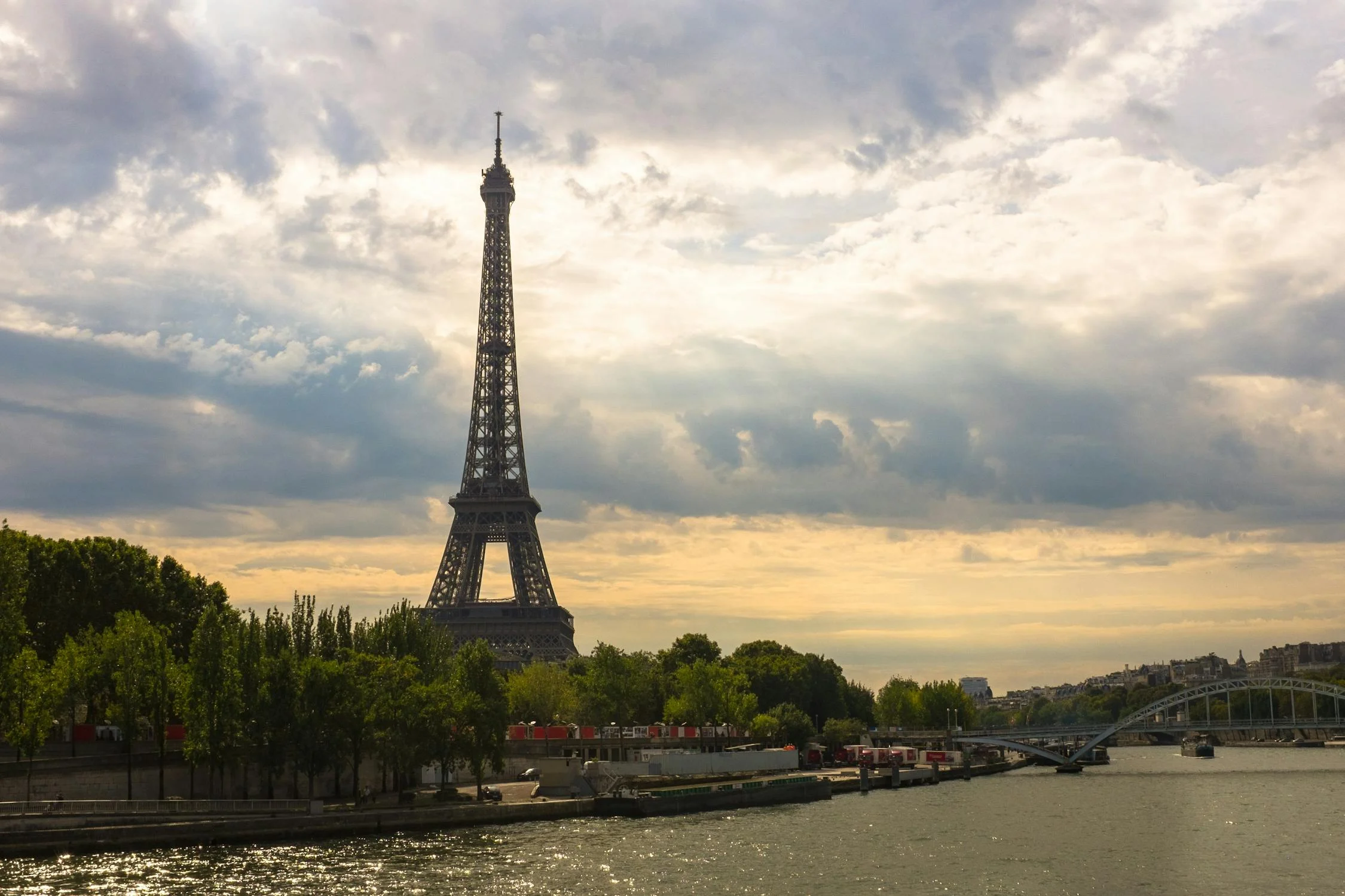 Eiffel Tower viewed from across the Seine River in Paris under a dramatic cloudy sky - Paris travel inspiration.
