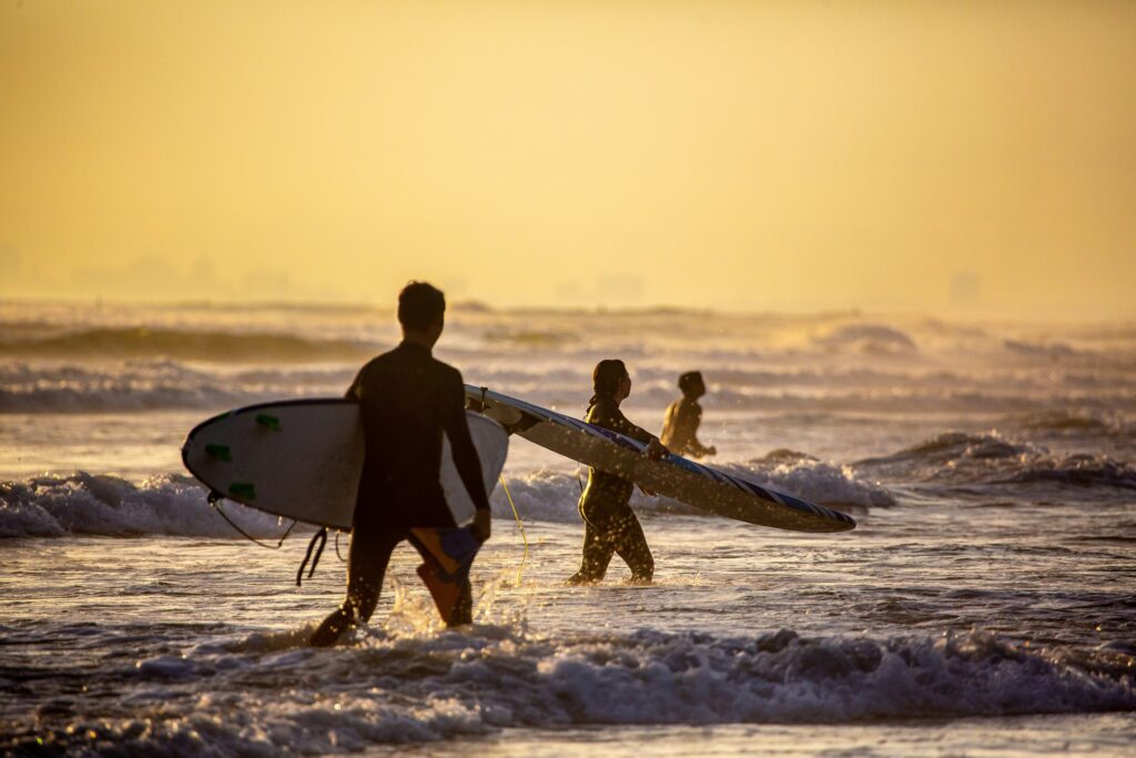 People surfing at the beach during sunset with ocean waves