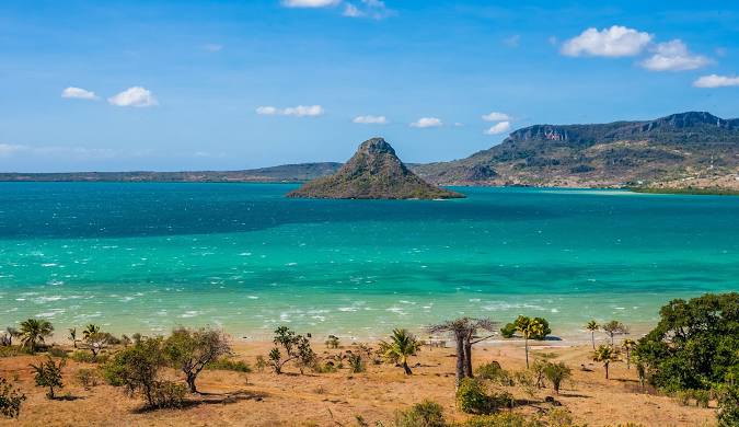 Turquoise waters lapping onto a pristine white sand beach in [Location, e.g., Nosy Be, Madagascar], with palm trees swaying in the breeze.