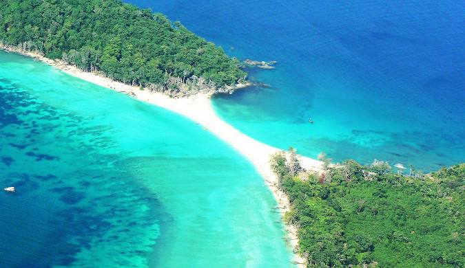 Aerial view of a Andaman Island lush, green island with a white sandy beach, surrounded by vibrant turquoise water.