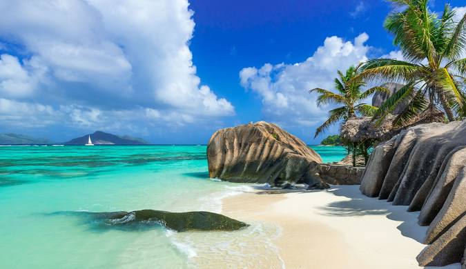 Paradise found in Seychelles: White sand beach with characteristic granite boulders, clear turquoise water, and swaying palm trees. Get the latest travel blog updates on Seychelles and plan your dream trip.
