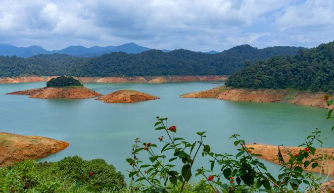 Scenic vista of Gavi Lake in Kerala, showcasing small islands dotting the turquoise water and surrounded by rolling hills covered in lush vegetation.