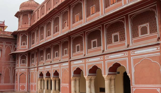 The detailed Rajasthani architecture of the Hawa Mahal's facade in Jaipur, viewed from below, showcasing the repetitive pattern of its iconic small windows and balconies in pink sandstone