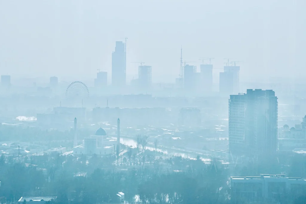 City skyline of Tashkent, Uzbekistan, shrouded in a light haze, featuring modern buildings, a Ferris wheel, and a mosque.