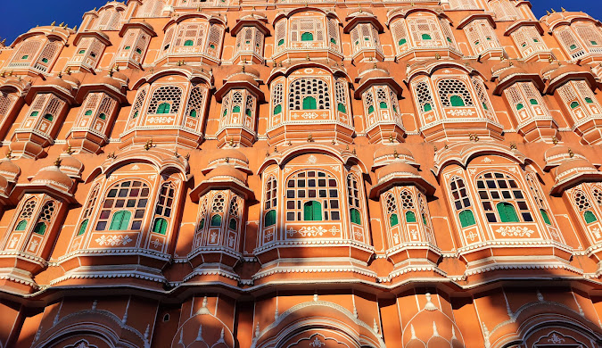 Low-angle view of the intricate pink facade of the Hawa Mahal in Jaipur, India, showing rows of small windows.