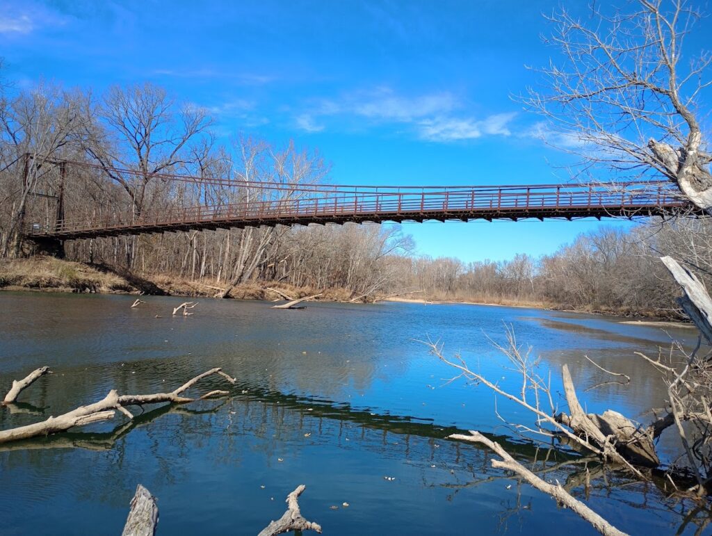 Suspension bridge over a river in a wooded area of Mark Twain National Forest. Discover unique trails and scenic bridges during your Ozark National Forest hiking adventure, adding to the exploration experience.