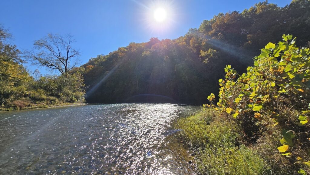 Sun shining through trees over a clear river in Mark Twain National Forest. Enjoy the tranquility of nature and crystal-clear rivers on your Mark Twain National Forest adventure, ideal for relaxation and exploration.