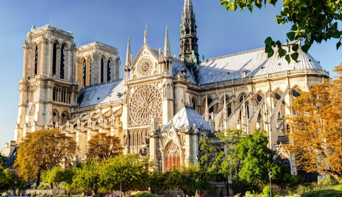 The intricate Gothic architecture of Notre Dame Cathedral in Paris, framed by green and autumn leaves - featured in travel blog articles.