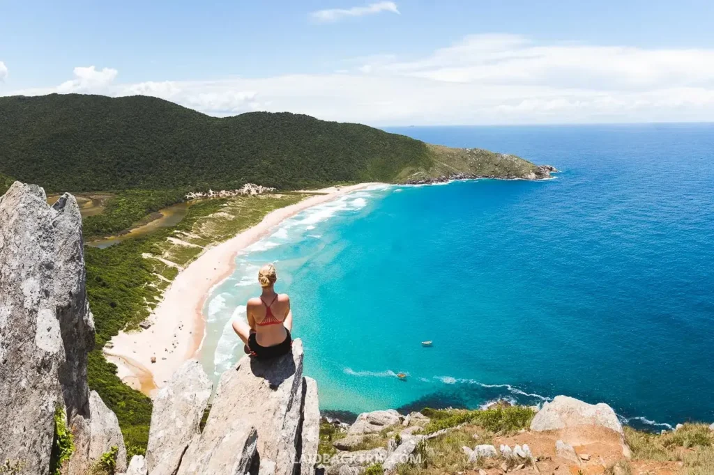 Hiker on rocky trail above Lagoinha do Leste, looking down at sand, lagoon and forest